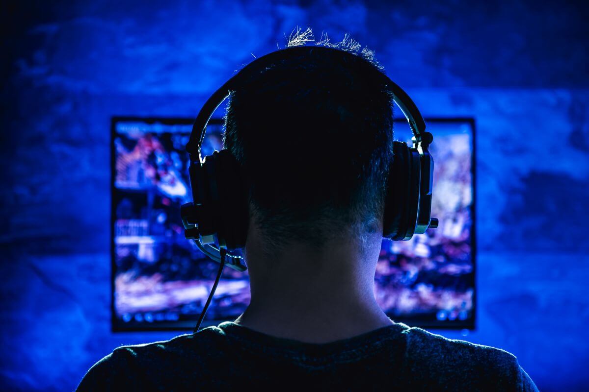 The picture of a man using a headset while watching on the computer refers to a freelance tester for video games as an easy way to earn money while doing something fun.