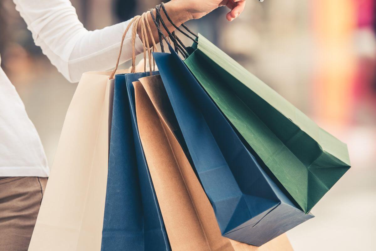 The photo tells about a girl's hand carrying shopping bags which means that adopting a one-year rule helps avoid impulse buys and keeps your money in your pocket for longer.