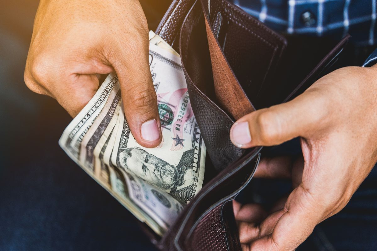 Picture of a man's hand putting his money in a wallet.