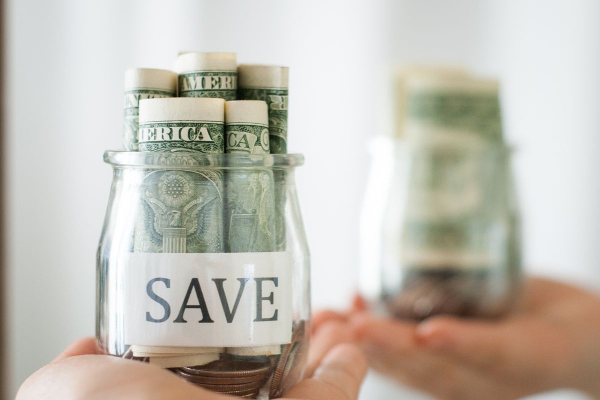 Picture shows a woman's hand holding a jar of savings.