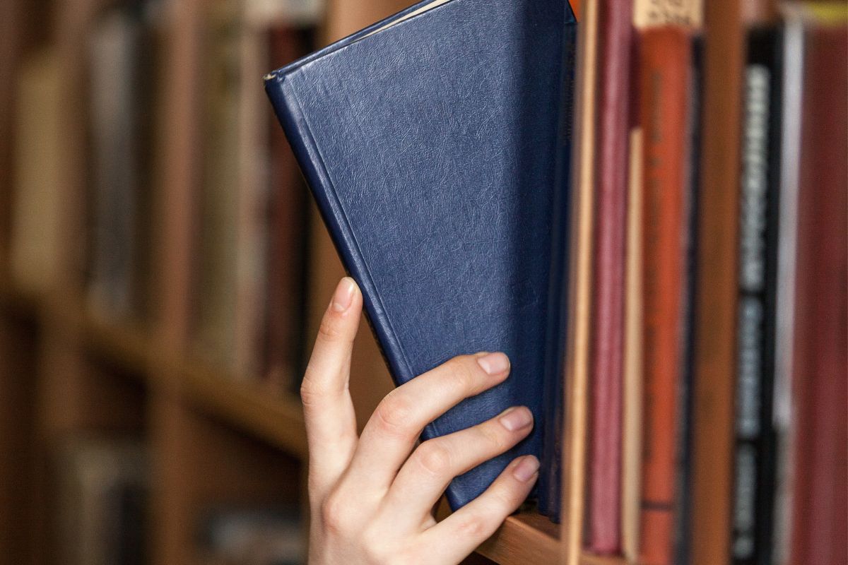 Picture a woman's hand and picking a book in a library.
