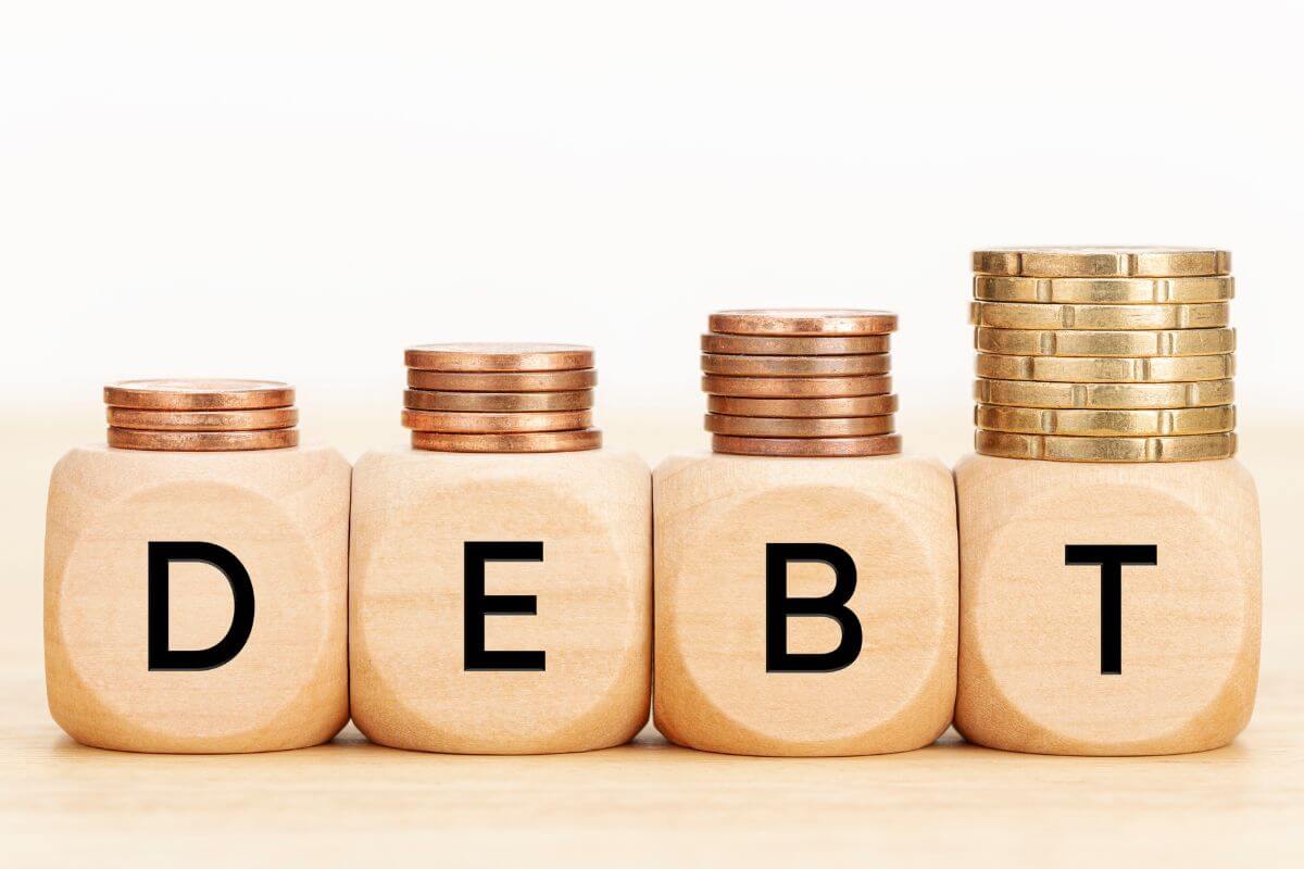 The image shows stock coins and wooden cubes with letters which refers to prioritizing paying off high-interest debt first helps reduce the amount you pay in interest over time.