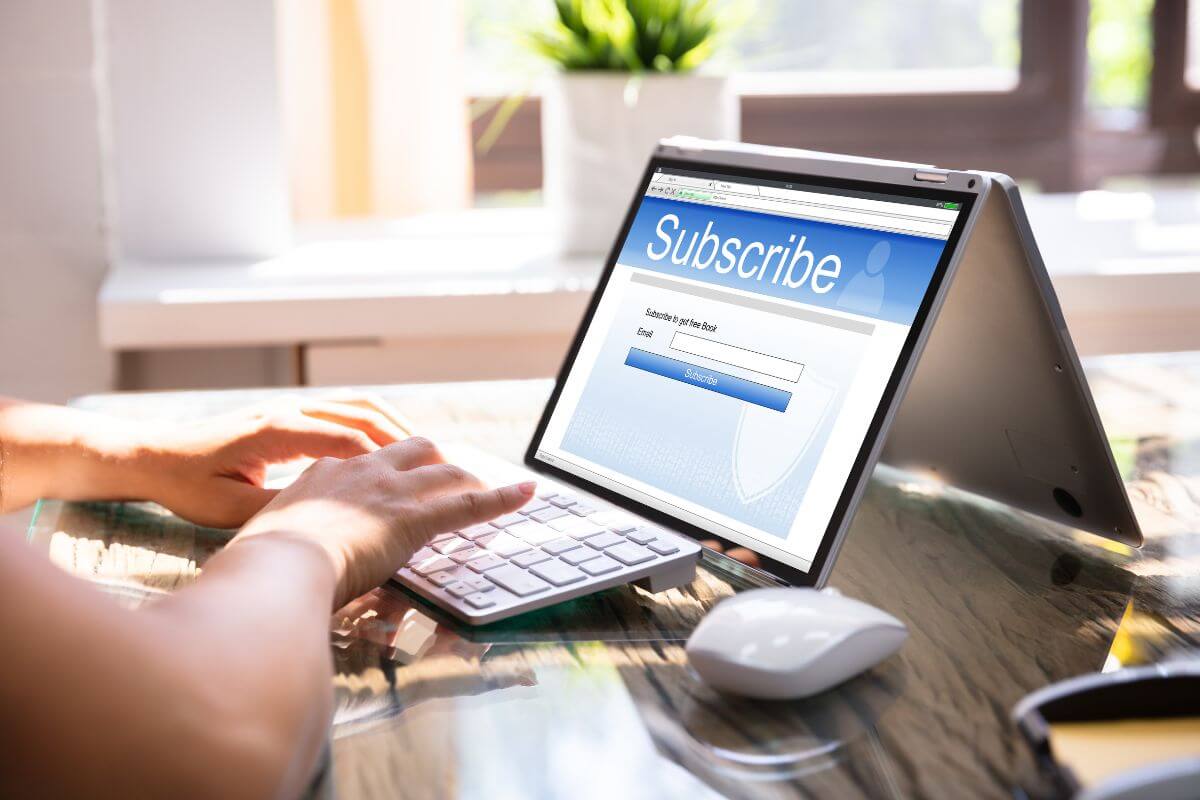 The image shows a girl's hand using a laptop with a screen display referring to cancel unused subscriptions helps you spend less and free up cash for more important goals.