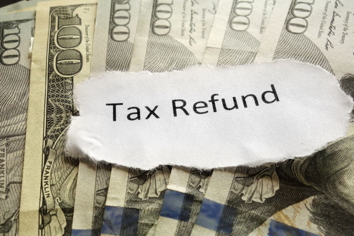 The picture of dollar bills and a piece of paper with notes referring to saving windfalls instead of spending them can boost your financial goals faster.