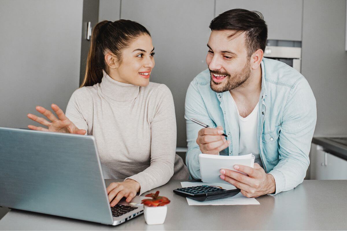The photo shows a calculator, a paper, and a girl using a laptop, and looking into the man to take down notes on what she said which means to get an accountability partner makes money management feel easier and more achievable.