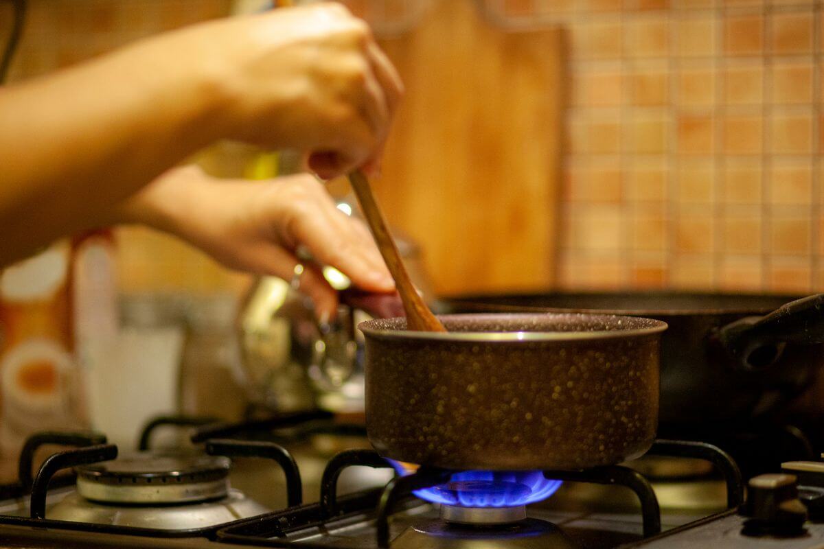 The photo tells about a girl mixing meals in a pan while on the stove to cooking meals at home and bringing leftovers to work saves a lot of money compared to eating out and keeps you in control of your spending.
