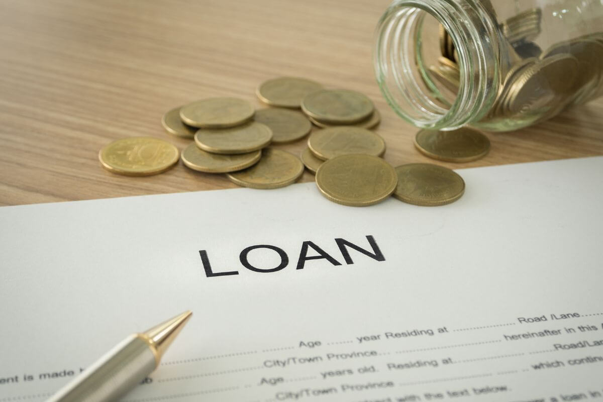 The image tells about a jar filled with coins, a pen, a paper with notes indicating that refinancing loans to reduce interest costs is a smart way to improve your overall financial health.