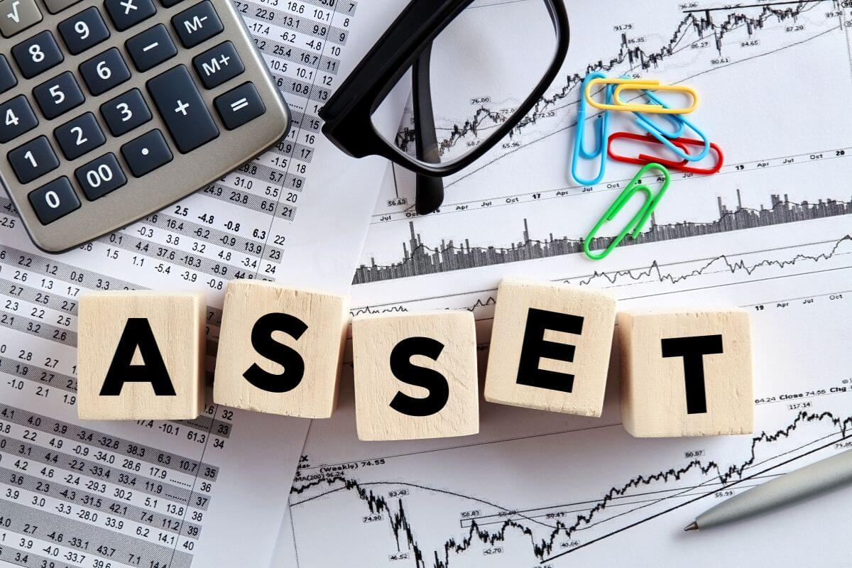 The picture tells about a calculator, an eyeglass, pins, papers with graphs and numbers, and wooden cubes with letters referring to investing in appreciating assets to ensure your money grows and supports your future goals.