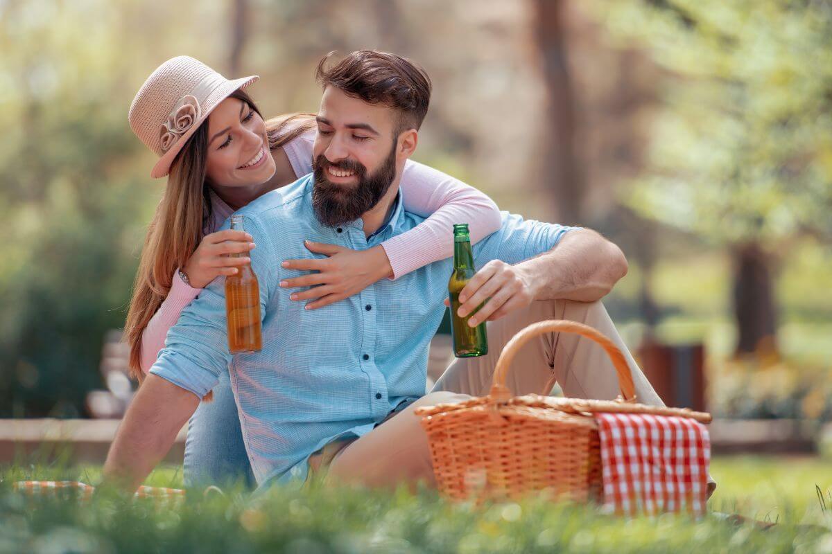 The image tells about a basket with clothes and a couple drinking together which means having a picnic in a local park, making food saving money, and adding a personal touch to the experience.