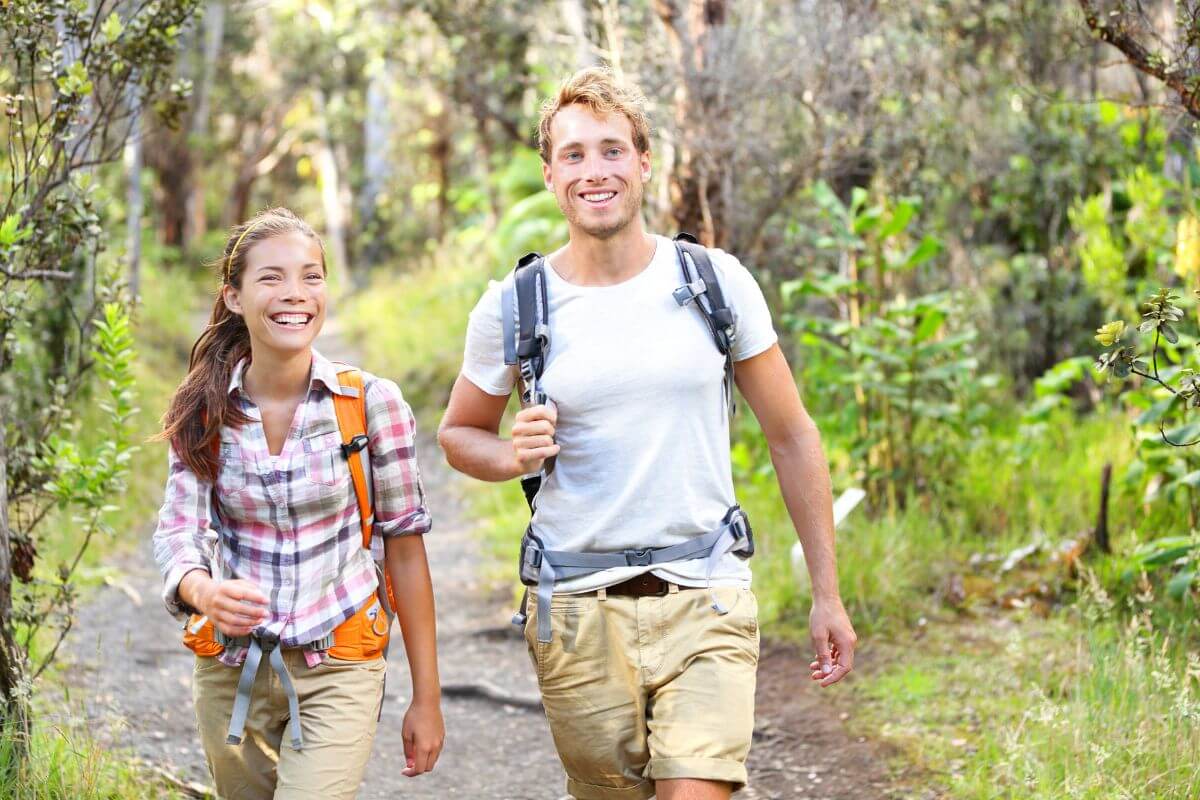 The image shows a couple with their backpacks enjoying walking together indicating that taking a scenic walk or hike is a great way to spend time together for free.