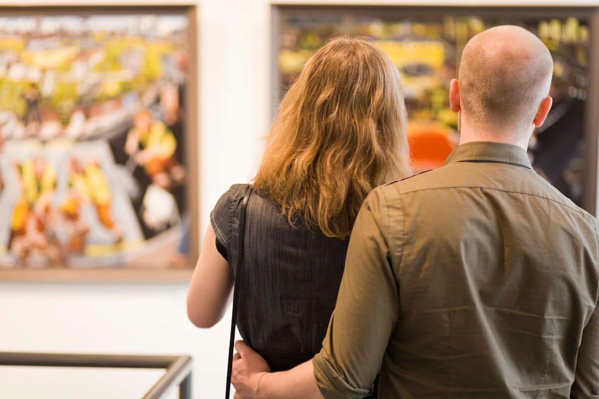 The photo shows a couple looking at the paintings referring to visiting a free museum gives you plenty to talk about and enjoy.