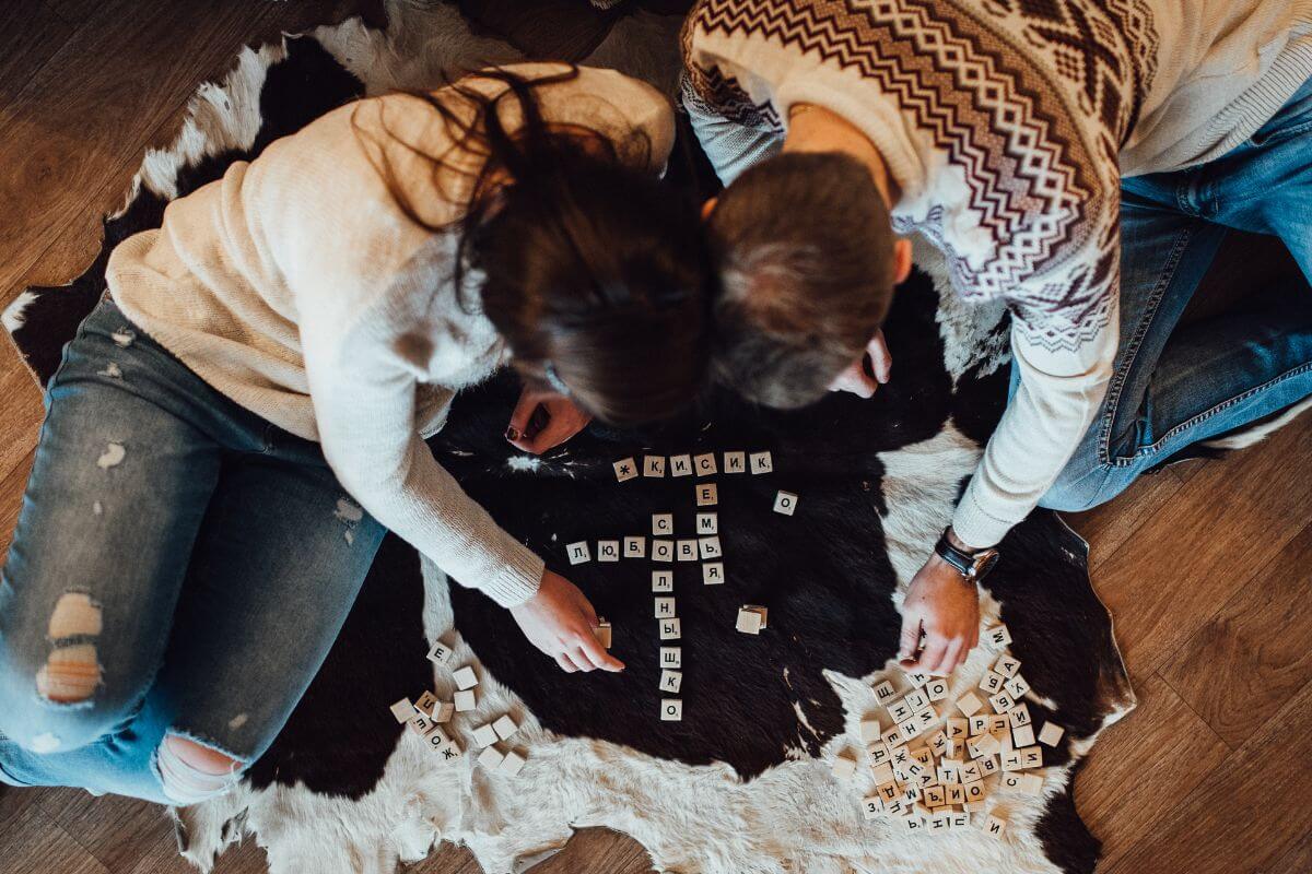 The picture shows a couple playing word puzzle which means to have a game night with your favorite board are a fun and inexpensive way to spend quality time.