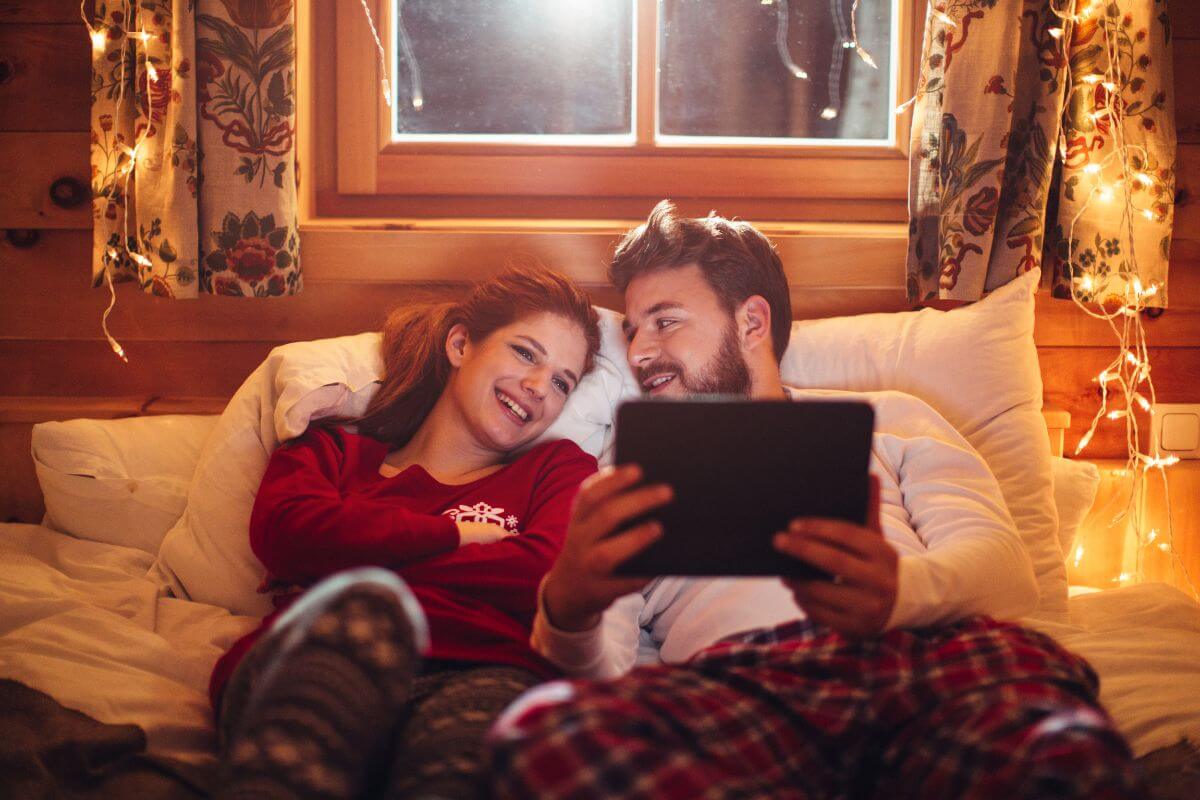 The picture of a couple watching on the tablet device a movie with good lighting means building a cozy fort indoors perfect for a date that's both intimate and easy on your wallet.