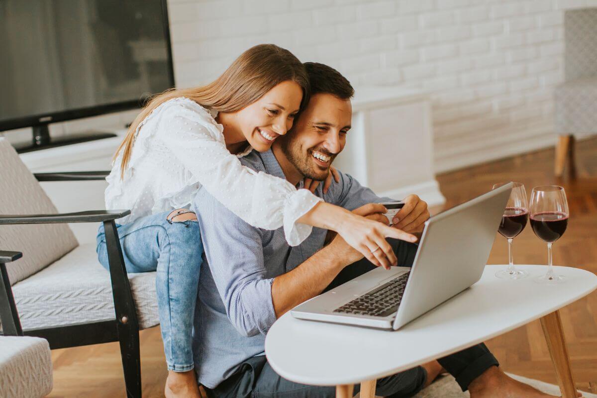 The image shows wine on the glass and a couple using a laptop indicating that picking up something small that won't break the bank can make your date feel extra special.