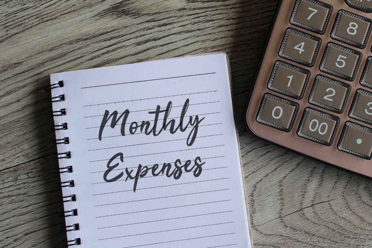 Picture of a calculator and a notebook with monthly expenses written.