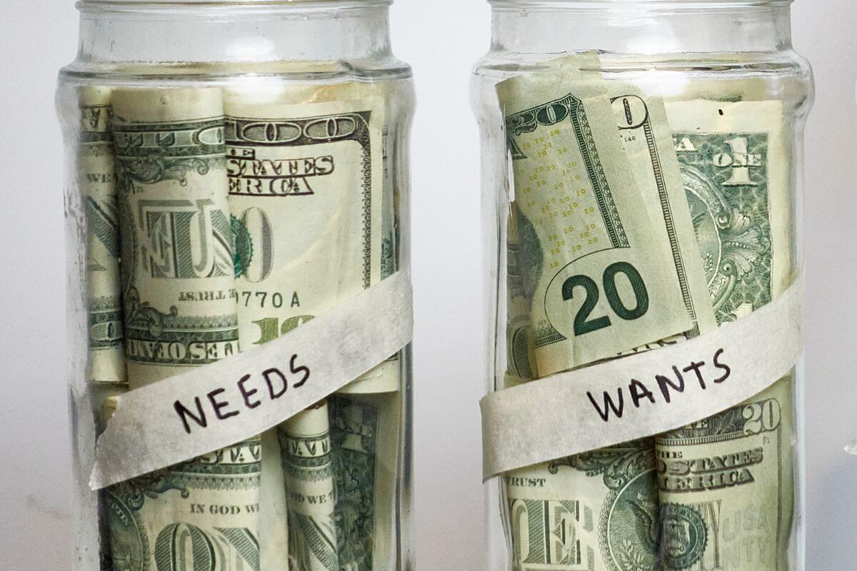 The picture shows jars filled with dollar bills and with notes referring to separate expenses into needs and wants helps you make smarter choices and cut back when needed.