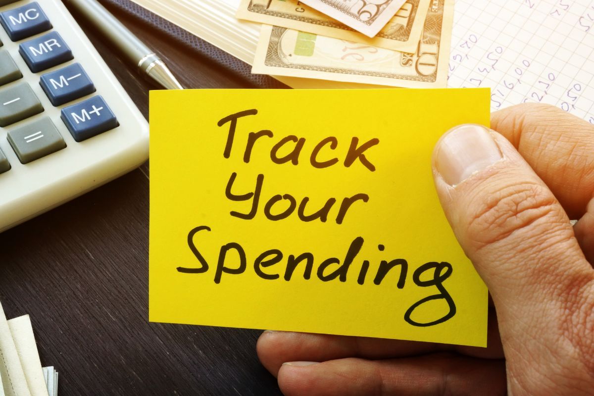 Photo of a man's hand holding a paper with Track your spending written.
