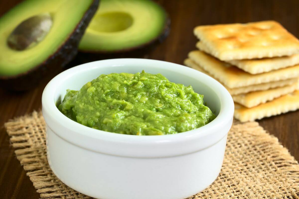 The photo of biscuits, sliced avocado, and a bowl with avocado cream referring to avocado-based dips cost way more than making them at home.
