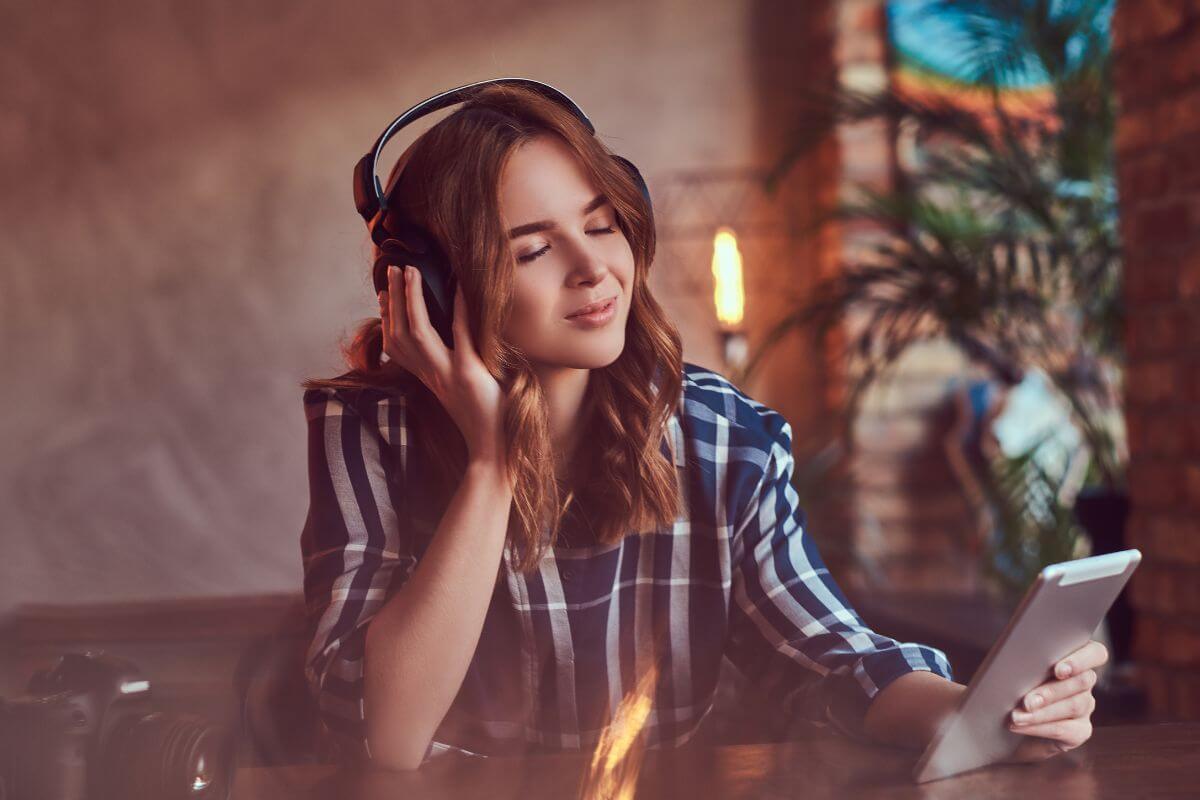 The image shows a girl holding a tablet device while listening through headphone which means a custom playlist of songs that remind you of them is simple yet meaningful gift for you partner.