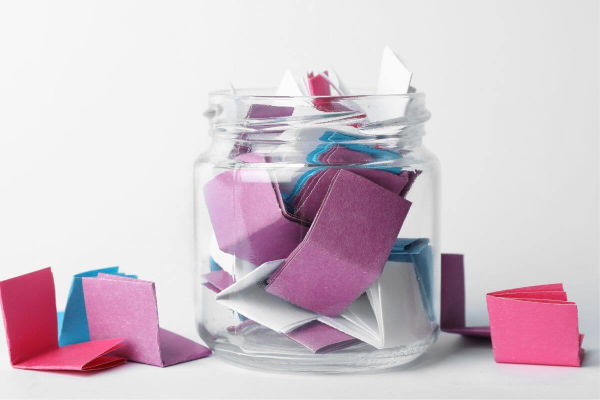 The photo shows a jar filled with small papers folded in different colors which means making a jar filled with notes of reasons you love them is a sweet personal gift for your partner.
