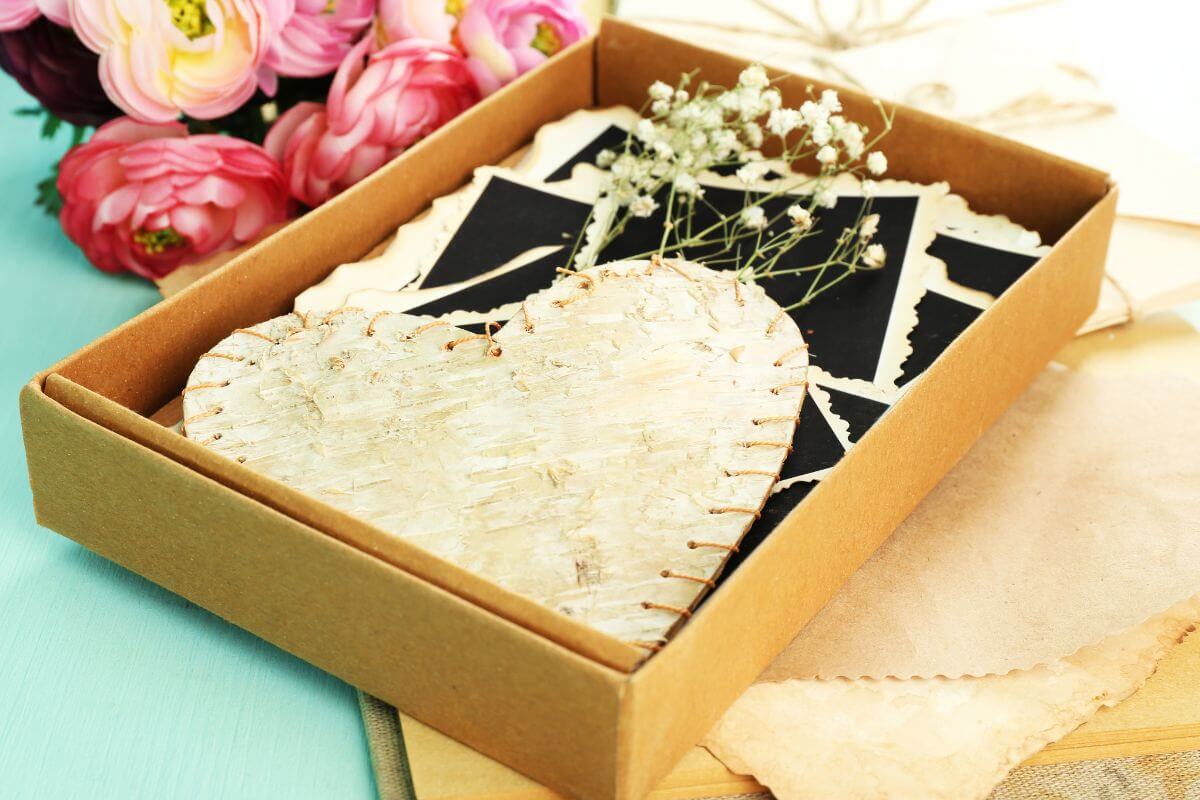 The photo shows a flower and a box filled with photos and a heart which means a memory box with mementos from your relationship makes a perfect keepsake that will only grow more special over time.