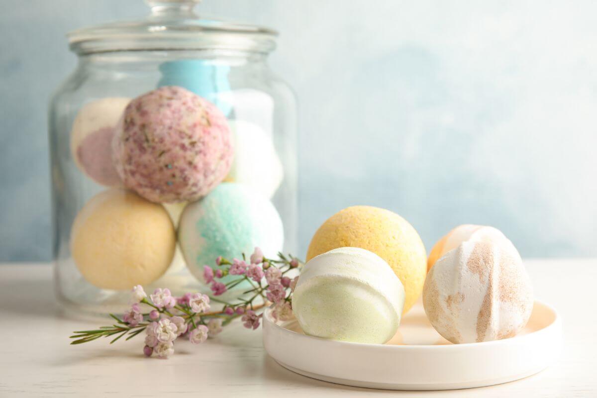 The picture tells about a jar and small plate filled with bath bombs and a flower indicating a DIY spa kit with homemade bath bombs which is a great way to give them a little self-care at home.