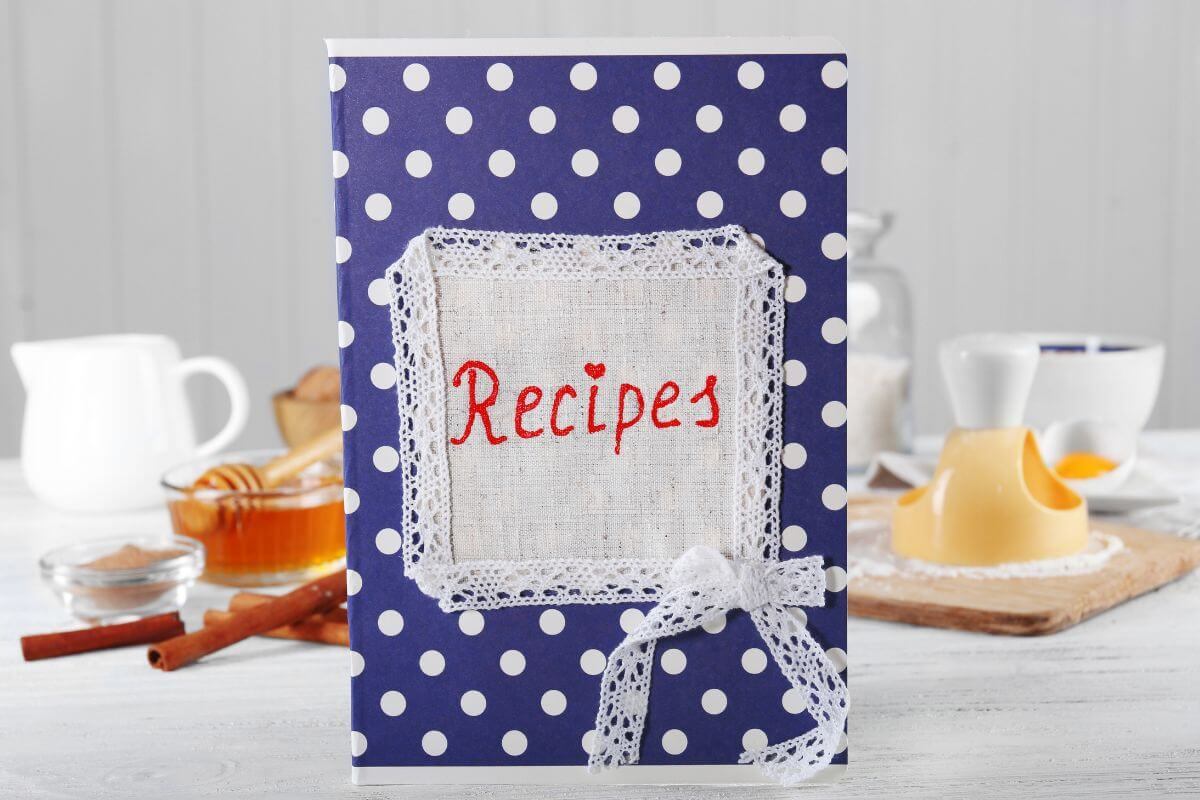 The photo shows ingredients behind and a book with a note and design which means giving a recipe book filled with meals you'd love to cook together which is a great gift for couples who love cooking.