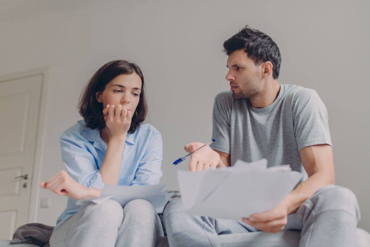 The picture tells about a man holding papers and pointing them to his partner which means that avoiding discussing finances can lead to hidden debts, financial stress, and misunderstanding.