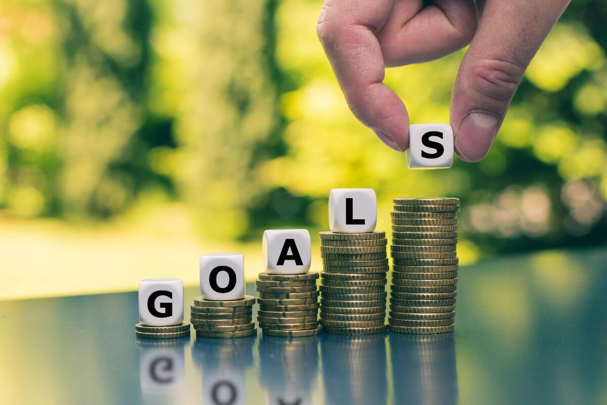The image tells about coin stocks, cubes with letters, and a man's hand putting the last letter referring to a lack of financial goals or savings plan may struggle with long-term stability.