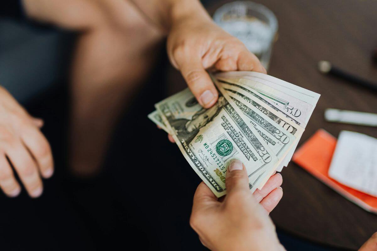 The picture shows a man's hand handing the dollar bills to the girl's hand which means borrowing money frequently without repaying it can mean they aren't managing their finances well.