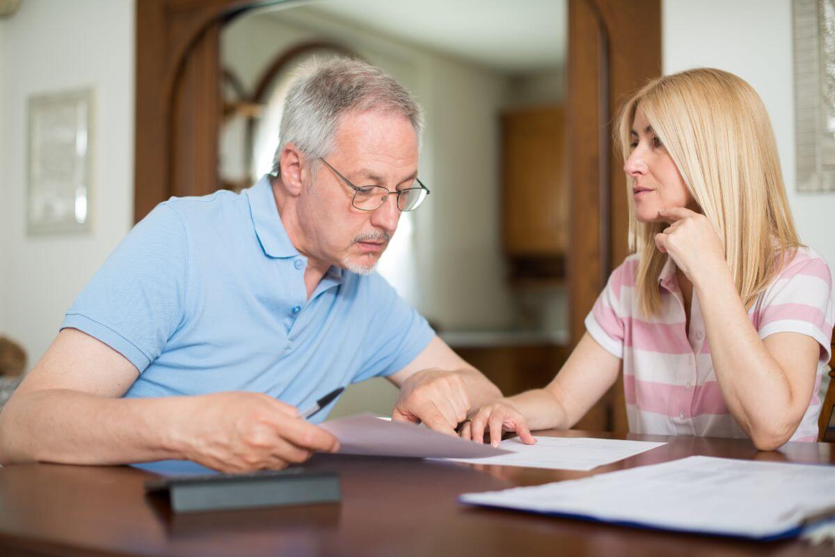 The picture shows a calculator, papers on the table, and a couple checking the papers referring to encourage them to calculate their monthly expenses to avoid overspending.