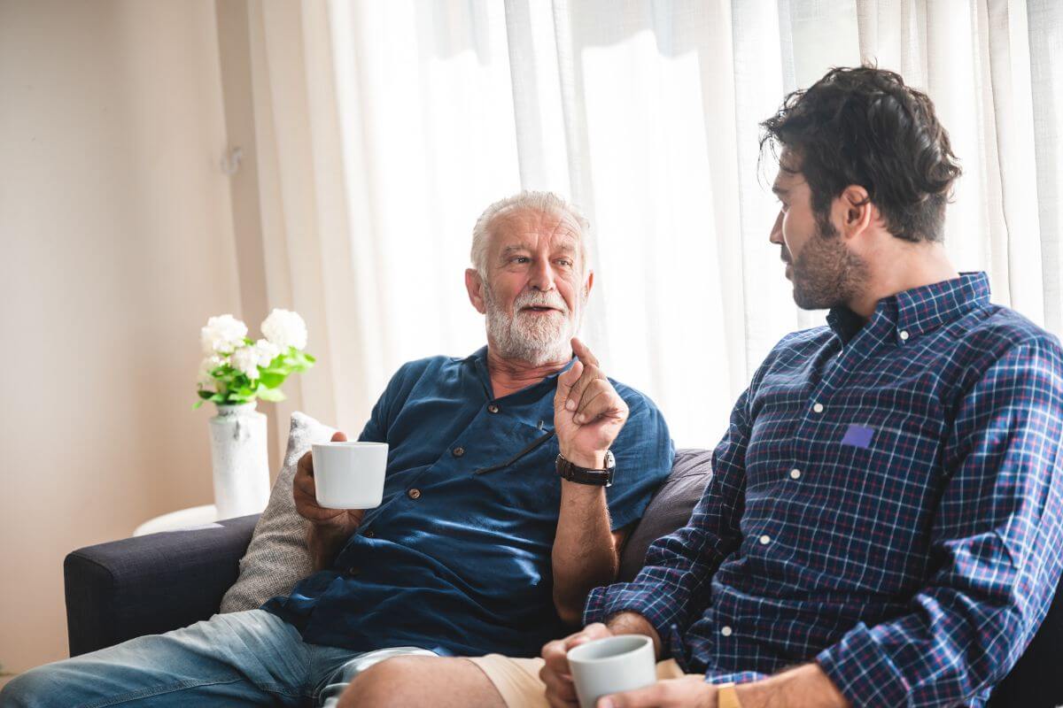 The picture shows a son and father talking together with coffee which means open conversations about their financial situation can help adjust their finances and set realistic expectations.