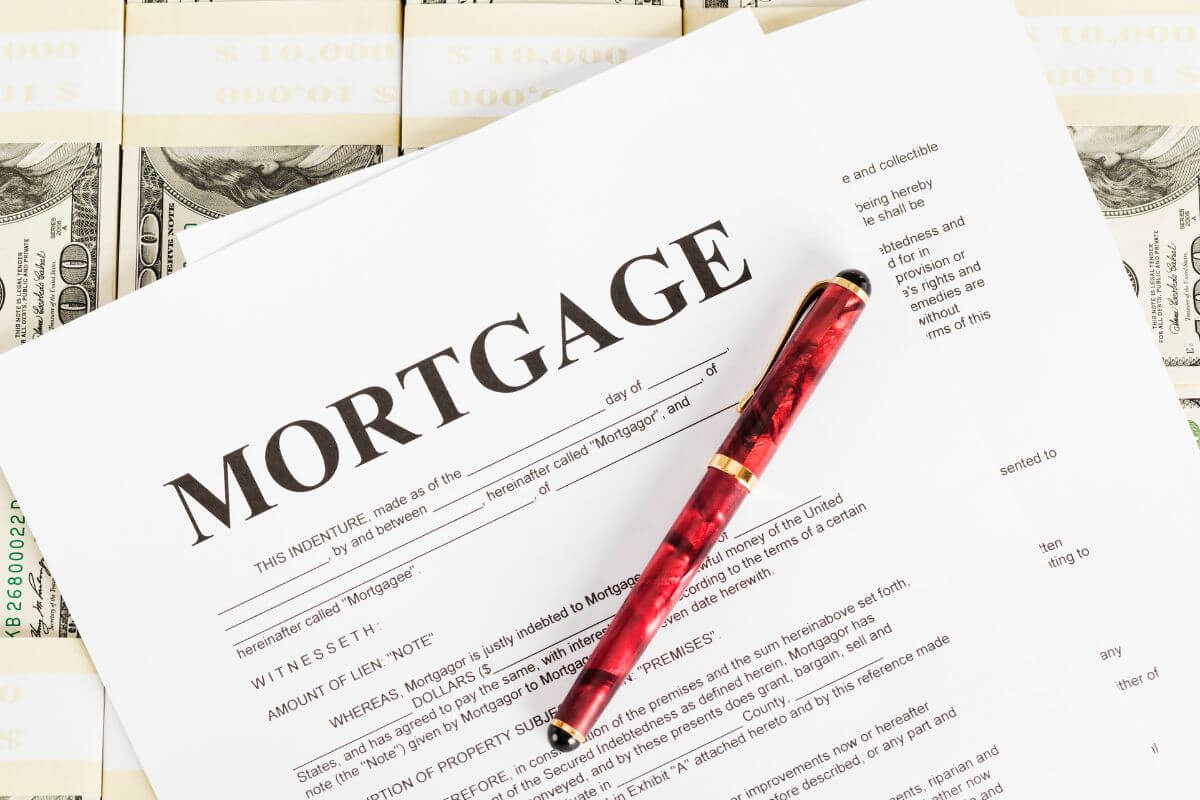 The image shows dollar bills, a pen, and papers with notes referring to carrying a mortgage or home loan into retirement, which means large monthly payments that eat into your savings.