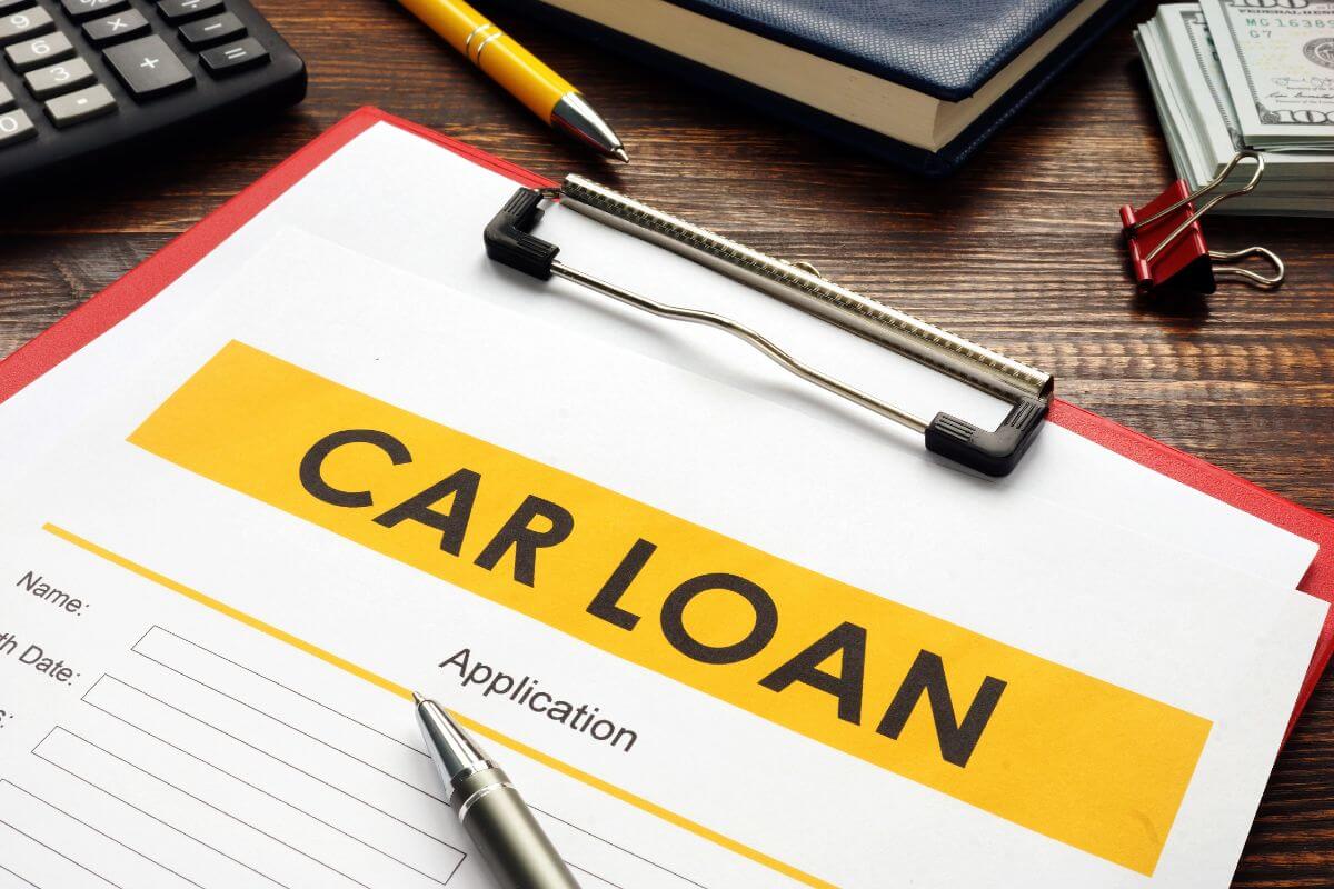 The photo shows a calculator, pens, a notebook, dollar bills, and a clipboard with notes which means auto loans can take a big bite out of your retirement budget.