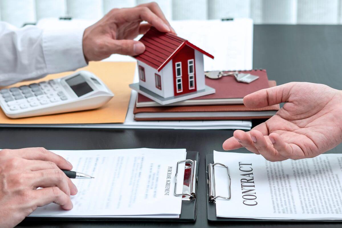 The image shows a calculator, notebook, a mini house, clipboards, and two man hands referring to co-signed loans that can hook your savings if the borrower stops paying, paying off your name from these loans before retirement prevents surprise financial hits.