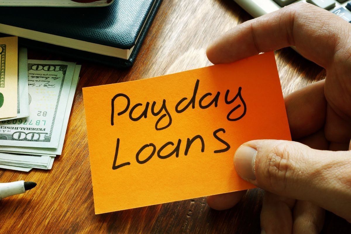 A man's hand holding a paper with payday loans written on it.