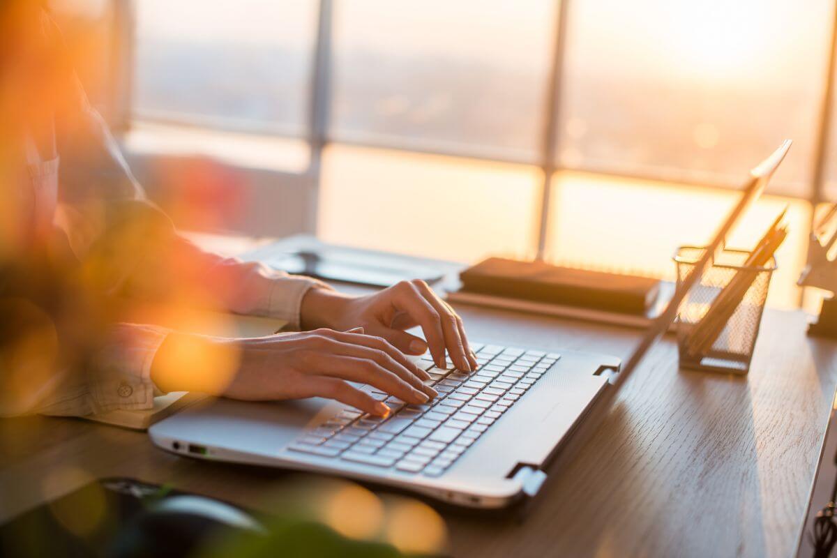 The photo shows pens, a notebook, and a girl's hand using a laptop which means unsubscribing from Marketing emails and avoiding shopping websites can prevent impulse purchases and help build a more frugal lifestyle.