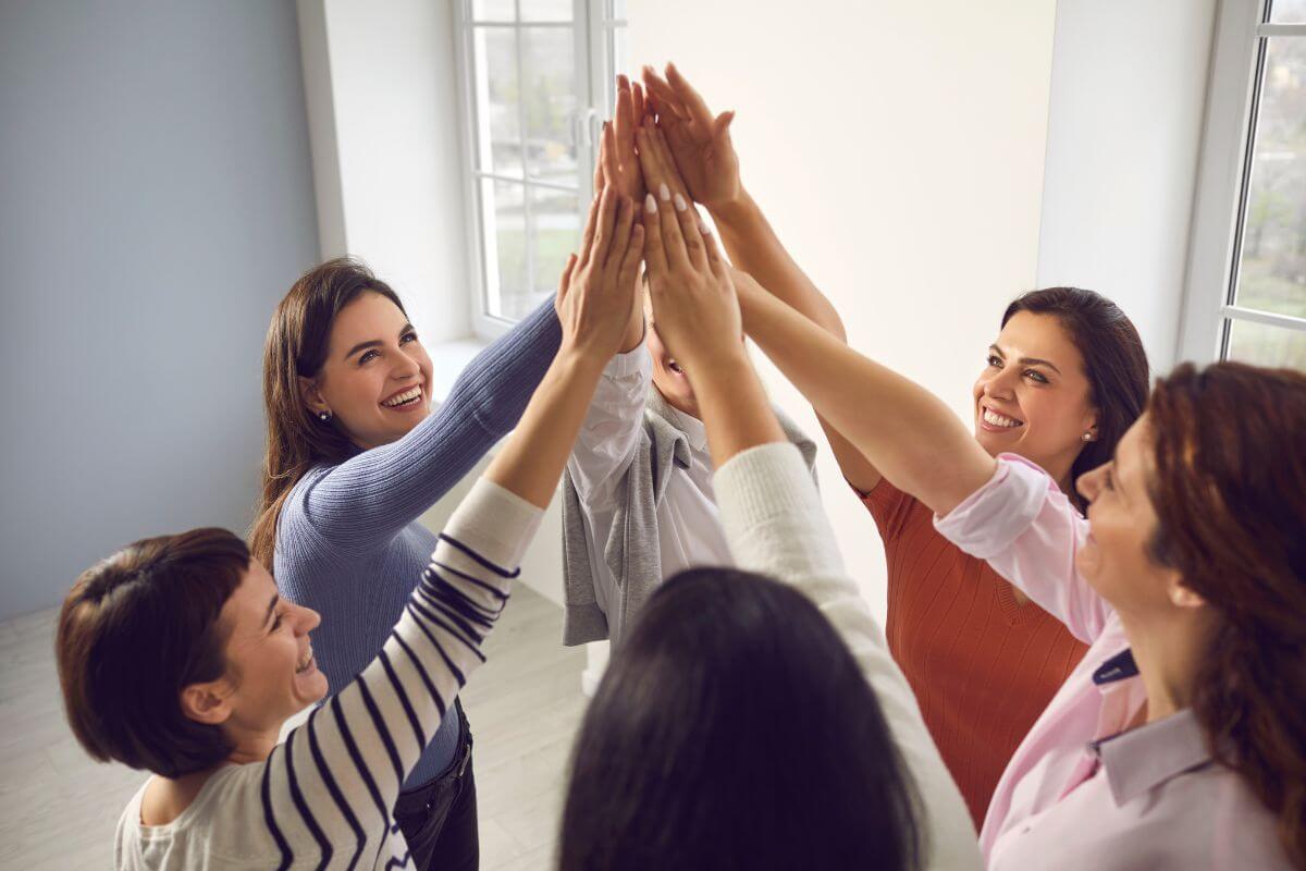 The image shows a group of women joining hands together indicating that joining a no-buy community for support can help stay on track.