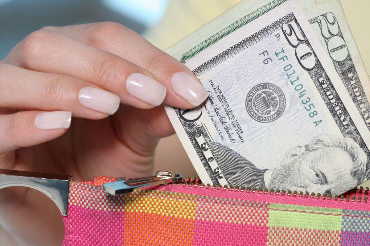 The image shows a girl's hand pulling out dollar bills on her wallet which means to reflect on spending habits can help break bad habits.