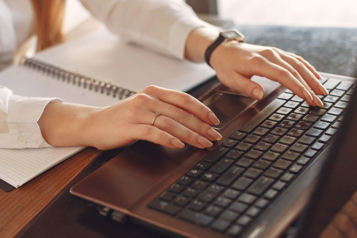 The image shows a notebook and a girl's hand using a laptop which means downloading your no-spend printables makes it easier to see how much money is being saved.