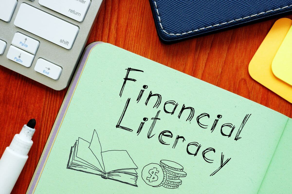 The image shows a keyboard, a notebook, a marker, and a paper with notes and illustrations, which means financial literacy is a skill that can be learned and can make a big difference in the future.