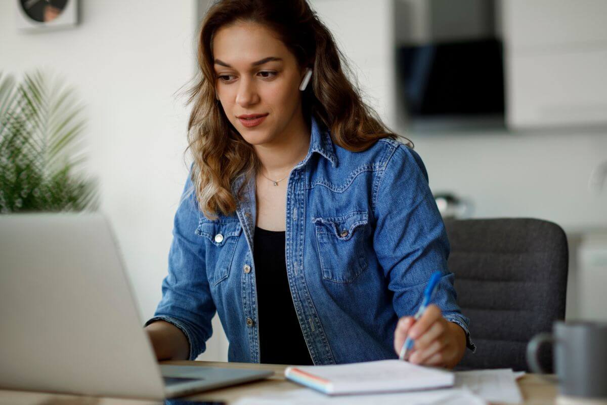 The photo of a girl looking at the laptop while taking down notes in the notebook refers to improving your financial skills by watching videos that can help you understand money better.