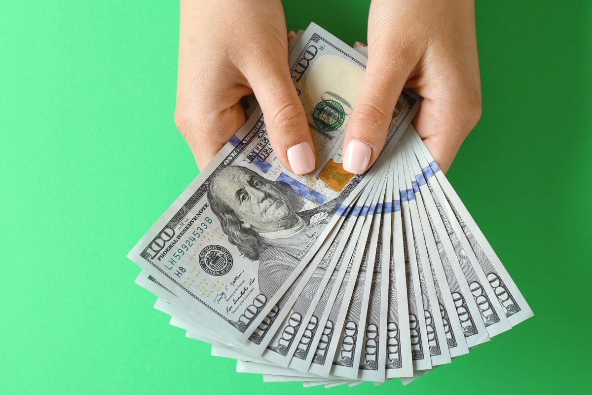 The image shows a girl's hand holding dollar bills which means focusing on financial discipline by cutting back on unnecessary purchases can bring financial freedom and less stress.
