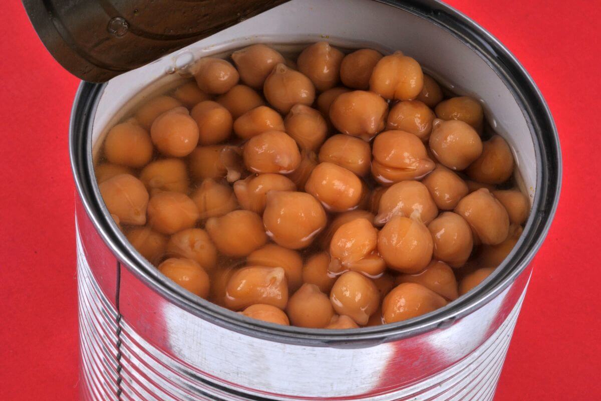 The image shows a can with chickpeas inside referring to canned beans with protein and fiber making them a cheap and filling option for meals to stock in your pantry. 
