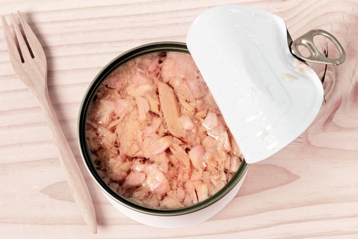 The image shows a wooden fork and canned tuna on the table indicating to some of the cheapest protein sources available and have long shelf life and easy meals when fresh meat isn't in the budget.