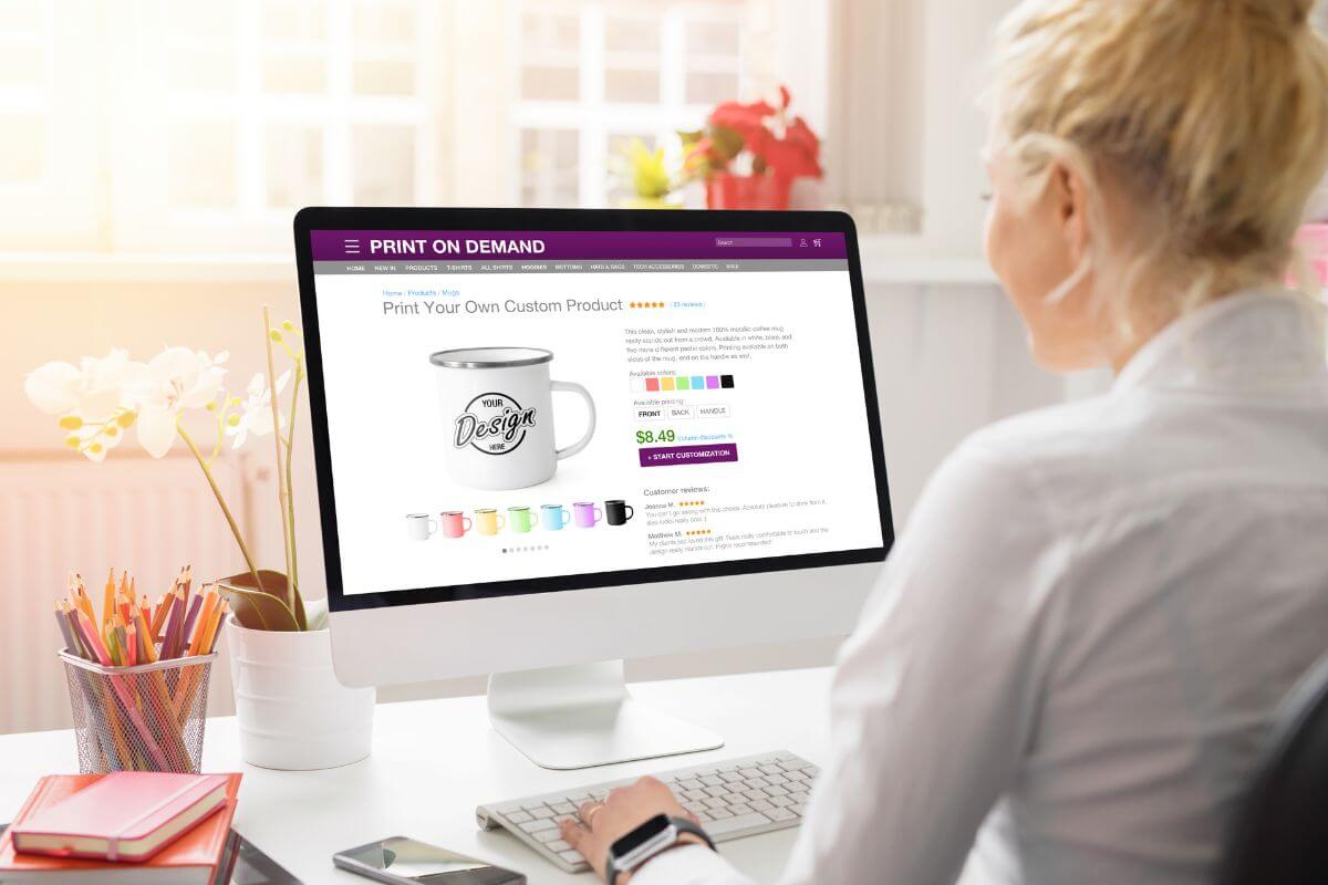 The picture shows pens, notebooks, a phone, and a girl using a computer with a screen display referring to selling digital products that can bring passive income from home.