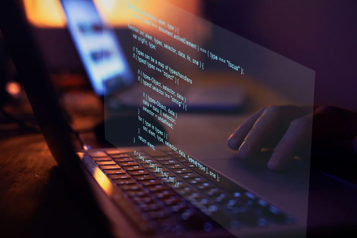 The picture of a man's hand using a laptop with a screen display indicates that software development is a high-paying job you can do from home.