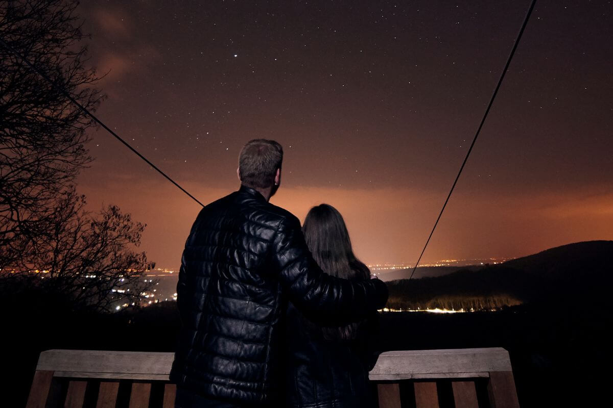 The image tells about a couple looking over the balcony referring to plan a memory like stargazing at home costs nothing but creates lasting memories.