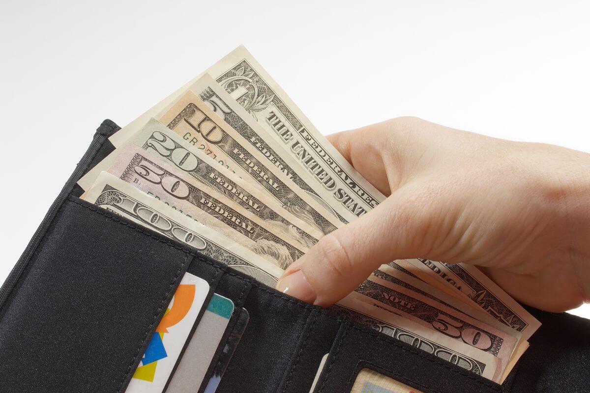 The image shows a girl's hand pulling dollar bills on the wallet with cards on it which means setting a spending limit on Valentine's day and focusing on thoughtful gestures that matter more.