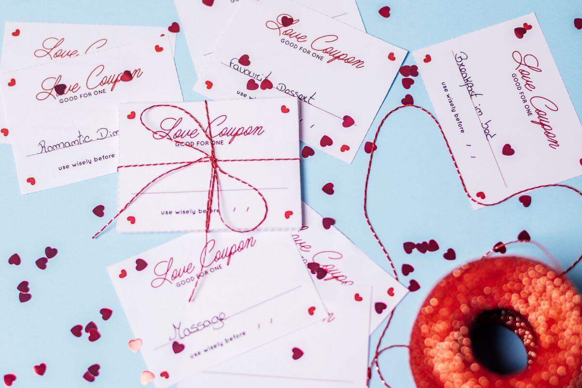 The picture shows papers with notes and heart sparkles with ribbon which means using free printables like love coupons that can make Valentine's Day feel special without spending a dime.